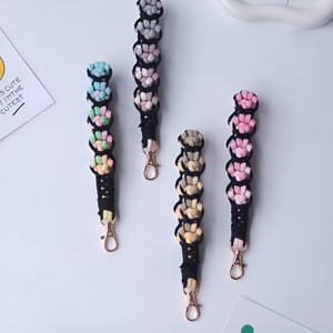 K&ouml;nnte beinhalten: F&uuml;nf bunte Schl&uuml;sselanh&auml;nger mit schwarzem Band und goldenen Schl&uuml;sselringen. Jeder Schl&uuml;sselanh&auml;nger besteht aus einer Reihe kleiner, flauschiger Bommeln in verschiedenen Farben.