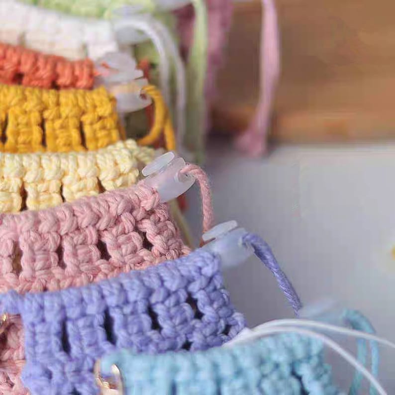 May include: A close-up of a stack of colorful crocheted yarn with plastic clips holding the yarn in place. The yarn is in shades of green, white, orange, yellow, pink, purple, and blue.