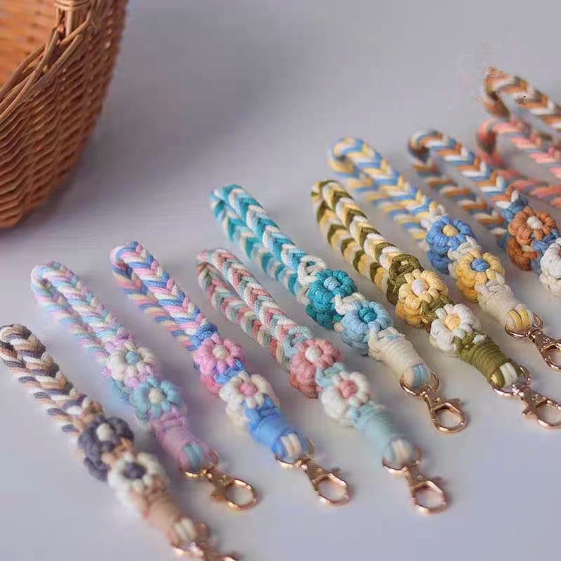 May include: A set of 10 colorful braided keychains with a flower charm at the end. Each keychain is made with a different color combination of yarn and has a gold metal clasp.