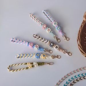 Könnte beinhalten: Fünf bunte geflochtene Schlüsselanhänger mit Blumenanhängern. Jeder Schlüsselanhänger hat eine andere Farbkombination und einen goldenen Metallverschluss.