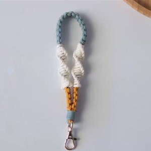 Pode incluir: Um chaveiro de macram&eacute; azul, branco e amarelo com um chaveiro prateado.