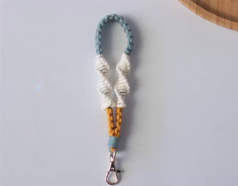 Pode incluir: Um chaveiro de macram&eacute; azul, branco e amarelo com um chaveiro prateado.