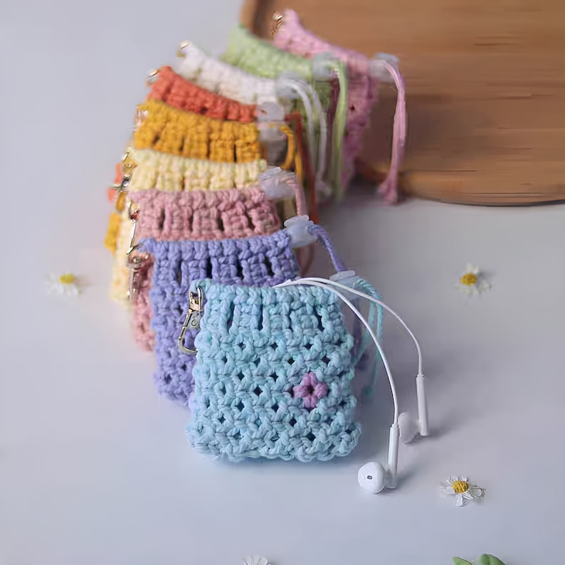 May include: A set of colorful crocheted pouches with a small flower detail. The pouches are lined up in a row and have a small metal clasp. The pouches are perfect for storing small items like earbuds or jewelry.