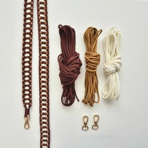 May include: A set of brown, tan, and white cords with gold metal clasps. The cords are arranged in a row on a white surface. The cords are likely for making a bag strap.