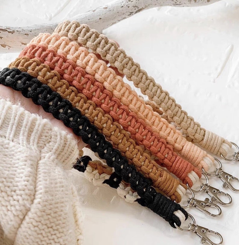 May include: A set of six colorful macrame cord keychains with black metal key rings. The cords are in shades of brown, orange, and pink.