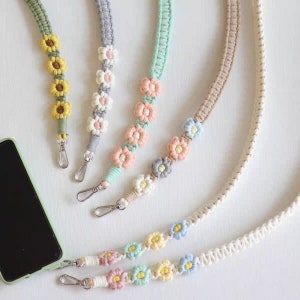 May include: Five colorful phone straps with flower accents. The straps are made of woven cotton and feature different colored flowers. The straps are attached to silver clasps.
