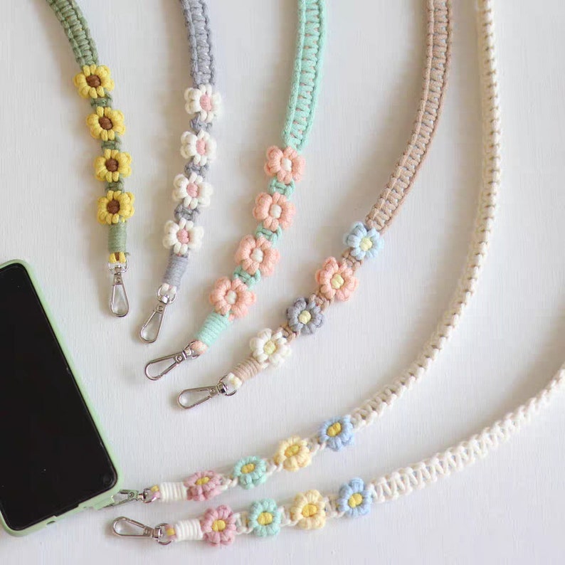 May include: Five colourful phone straps with flower accents. The straps are made of woven cotton and feature different coloured flowers. The straps are attached to silver clasps.