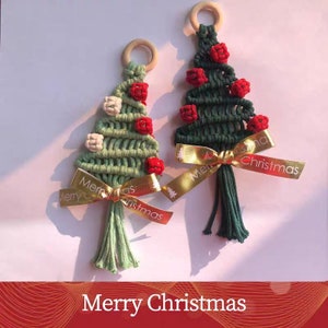 Op de afbeelding: Twee groene en witte macram&eacute; kerstboomversieringen met rode kralen en gouden lintjes. De ornamenten hebben de tekst "Merry Christmas" op het lint.