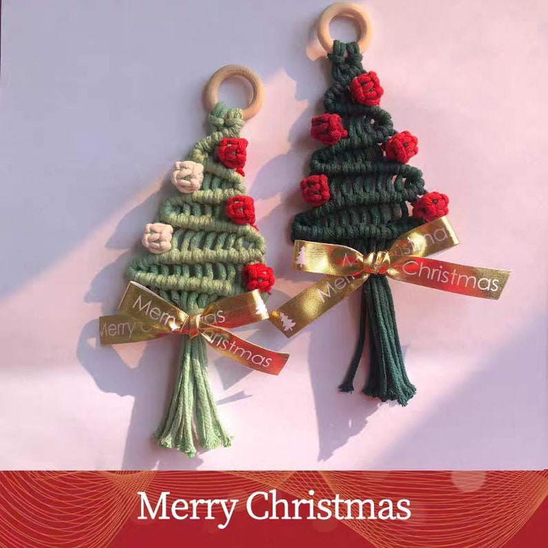 Op de afbeelding: Twee groene en witte macram&eacute; kerstboomversieringen met rode kralen en gouden lintjes. De ornamenten hebben de tekst "Merry Christmas" op het lint.