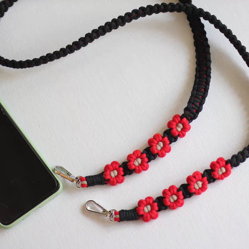 May include: Black phone strap with red and beige flower accents. The strap has two silver clasps.