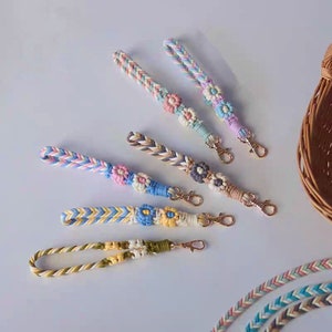 Peut inclure: Cinq porte-clés tressés colorés avec des accents de fleurs et des anneaux dorés. Les porte-clés sont faits de différentes couleurs, dont le rose, le bleu, le jaune et le vert.