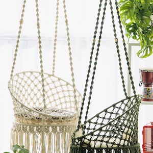 May include: Two macrame hanging chairs, one white and one green, with fringe trim. Both chairs have a cushion and are hanging from the ceiling.