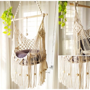 Peut inclure: Un fauteuil suspendu en macramé blanc avec un coussin brun. Le fauteuil est suspendu à une barre en bois et possède de longues franges.