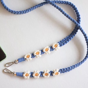 May include: A blue and white phone strap with daisy flower accents. The strap has two metal clasps.