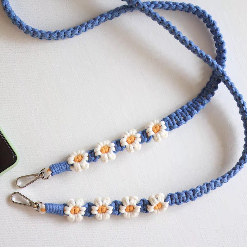May include: A blue and white phone strap with daisy flower accents. The strap has two metal clasps.
