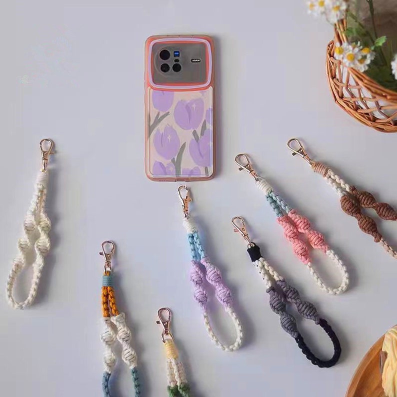 Puede incluir: Una colecci&oacute;n de correas de tel&eacute;fono coloridas con varios patrones y colores, incluyendo blanco, azul, rosa, marr&oacute;n y gris. Las correas est&aacute;n hechas de cuerda tejida y tienen un broche de metal.