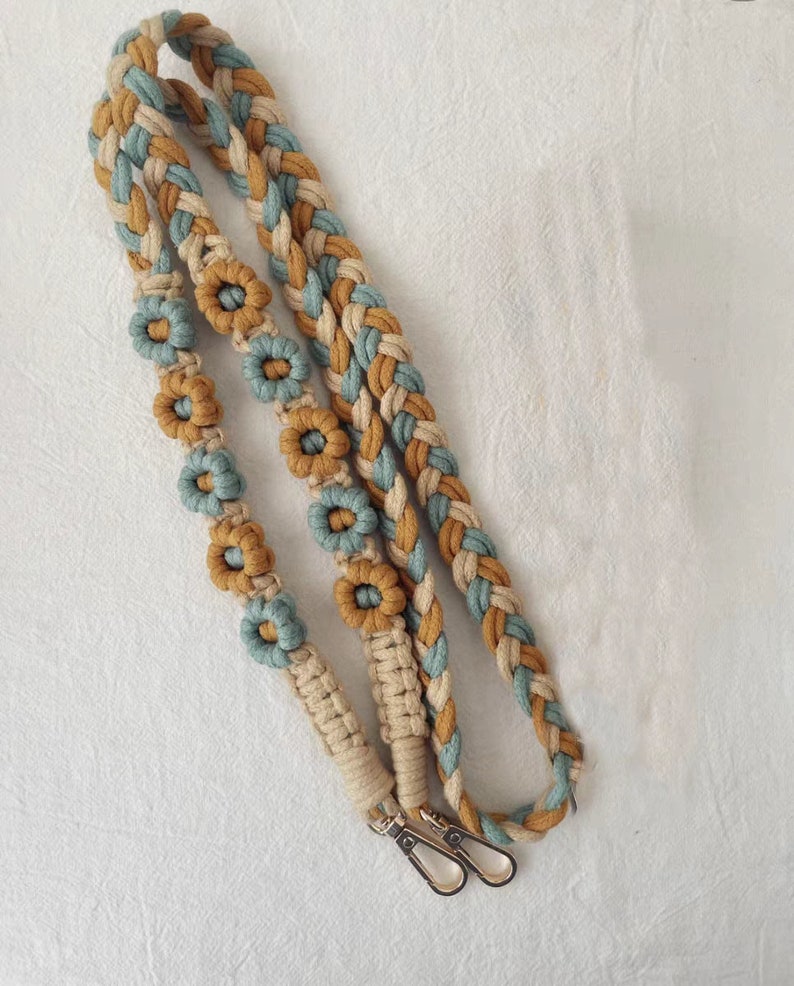 May include: A braided cotton strap with a light blue and beige pattern and brown flower accents. The strap has two gold metal clasps.