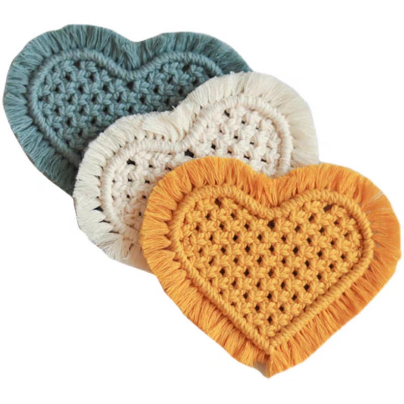 K&ouml;nnte beinhalten: Drei geh&auml;kelte Untersetzer in Herzform in den Farben T&uuml;rkis, Wei&szlig; und Gelb mit Fransen an den R&auml;ndern.