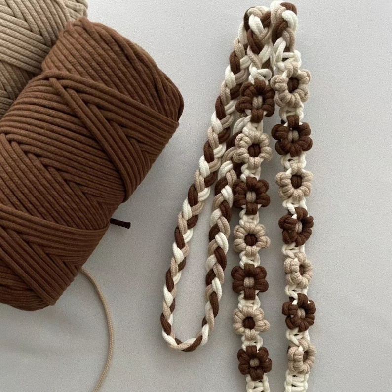 May include: A close-up of a brown and cream macrame cord with a braided design. The cord is decorated with brown and cream flowers.