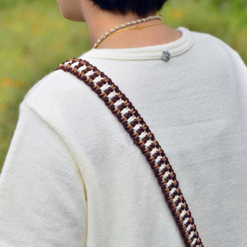 May include: A white shirt with a brown and white braided strap. The strap is worn over the shoulder and is a popular style for bags and purses.