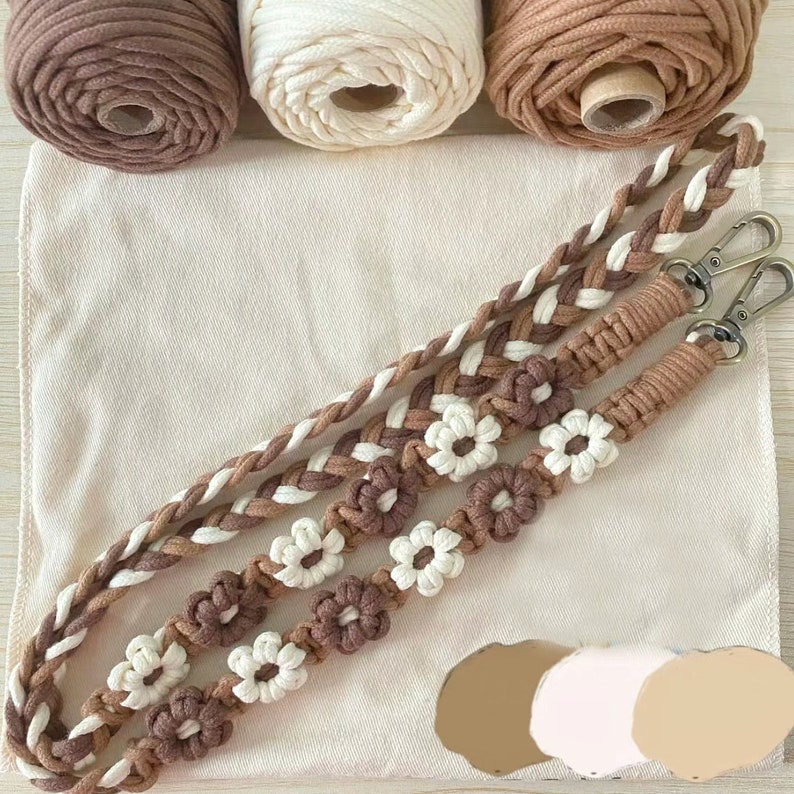 May include: A brown, white, and beige macrame strap with a flower design. The strap is made with three different colors of cord and is braided together.