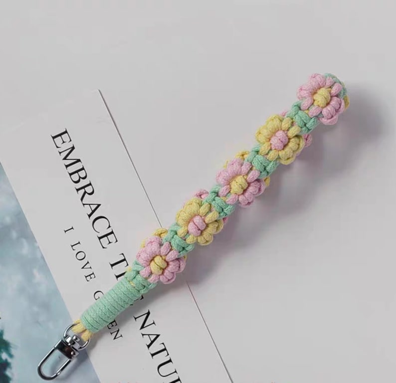 Może przedstawiać: Zielony, r&oacute;żowy i ż&oacute;łty brelok do kluczy wykonany na szydełku z motywem kwiatowym. Brelok ma metalowy pierścień na końcu.