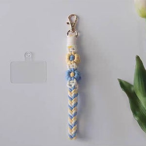 Pu&ograve; includere: Un portachiavi intrecciato bianco e blu con tre accenti di fiori gialli e blu. Il portachiavi ha una chiusura in metallo dorato e un porta carte in plastica trasparente.