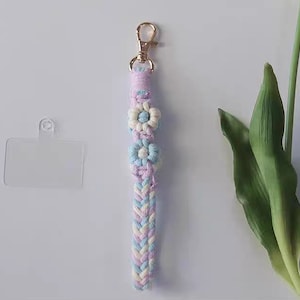 Pu&ograve; includere: Un portachiavi intrecciato rosa, blu e bianco con tre ciondoli a forma di fiore. Il portachiavi ha una chiusura in metallo dorato.