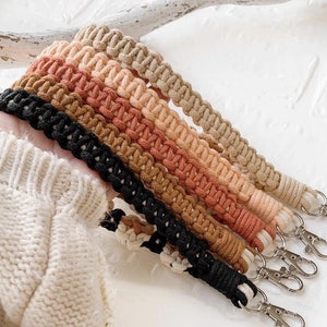 May include: A set of six colorful macrame cord keychains with black metal key rings. The cords are in shades of brown, orange, and pink.