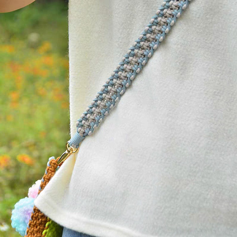 May include: A close-up of a light blue and beige braided strap with a gold metal clasp. The strap is attached to a white shirt.