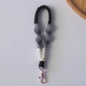 Pode incluir: Um chaveiro de macram&eacute; preto, branco e cinza com um aro de chave prateado.