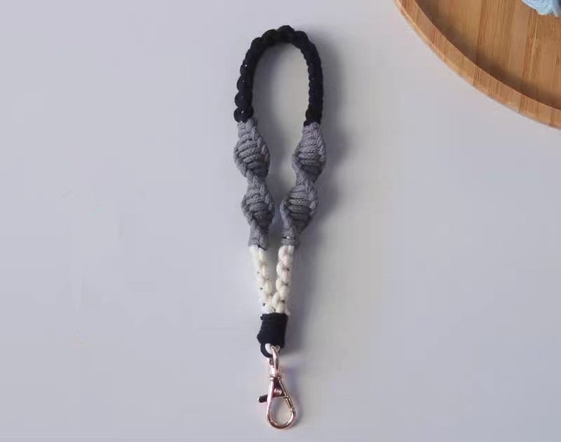 Pode incluir: Um chaveiro de macram&eacute; preto, branco e cinza com um aro de chave prateado.