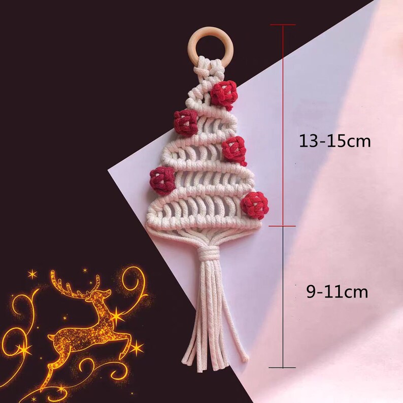 Op de afbeelding: Witte macram&eacute; kerstboom ornament met rode pompoenen en een houten ring aan de bovenkant. De ornament is 13-15 cm hoog en 9-11 cm breed.