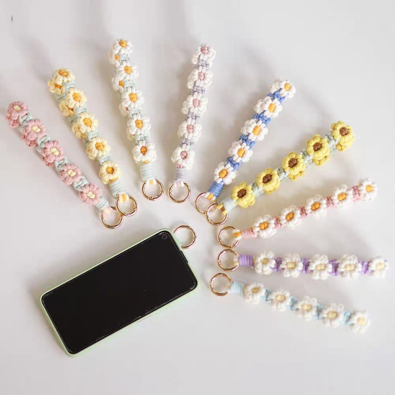 Puede incluir: Un conjunto de ocho llaveros con forma de margarita de colores con anillas doradas. Los llaveros est&aacute;n hechos de cuerda trenzada y presentan un patr&oacute;n de margarita en varios colores, incluyendo rosa, azul, amarillo y blanco.