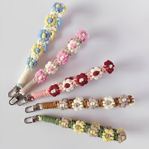 Może przedstawiać: Cztery kolorowe breloczki z kwiat&oacute;w na szydełku ze srebrnymi zapięciami. Breloczki są wykonane z przędzy w r&oacute;żnych kolorach i mają serię kwiat&oacute;w na szydełku.