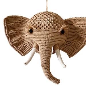 May include: A beige crocheted elephant head wall hanging with white tusks and black eyes.