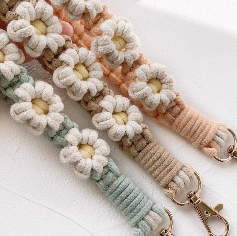 May include: Three crocheted keychains with daisy flower designs in shades of beige, light brown, and green. Each keychain has a gold metal clasp.
