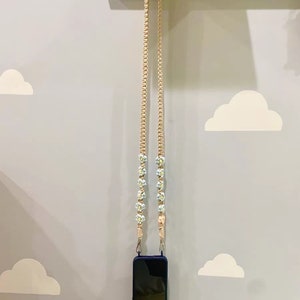 May include: A beige phone strap with blue and white flower accents. The strap is hanging from a pegboard wall.