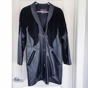 Może przedstawiać: Długi czarny płaszcz skórzany z kołnierzem ze skóry zamszowej i pojedynczym zapięciem na guzik. Płaszcz ma dwie kieszenie z przodu i metkę z napisem "Rumors".