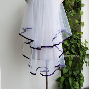 May include: White bridal veil with a single layer of tulle and a purple satin ribbon trim. The veil is displayed on a mannequin.