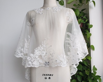 May include: White lace bridal shrug with beaded embellishments. The shrug is on a white dress form.