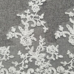 May include: White lace trim with a delicate floral pattern. The lace features intricate swirls and small flower designs.