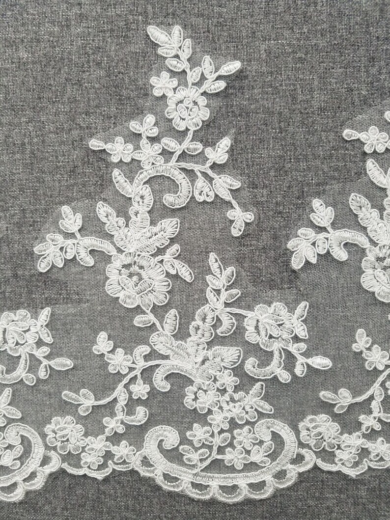 May include: White lace trim with a delicate floral pattern. The lace features intricate swirls and small flower designs.