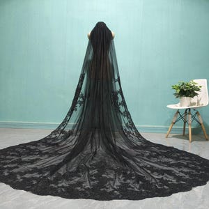 May include: A black lace wedding veil with a long train. The veil is made of delicate lace and has a scalloped edge.
