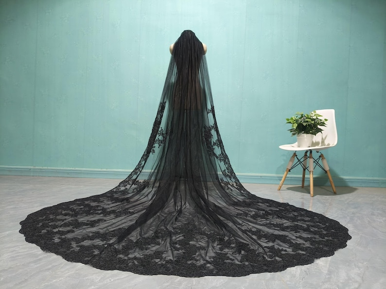 May include: A black lace wedding veil with a long train. The veil is made of delicate lace and has a scalloped edge.
