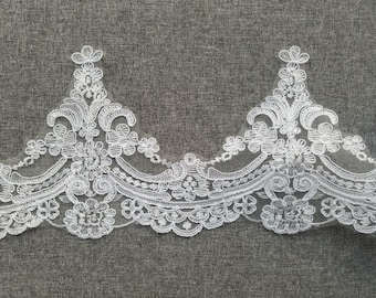 May include: White lace trim featuring a delicate floral design. The lace has a scalloped edge and is ideal for adding a touch of elegance to any project.