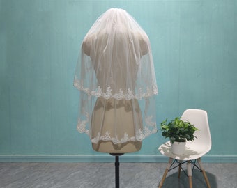May include: A white two-tiered bridal veil with lace trim. The veil is displayed on a white mannequin against a light blue background.