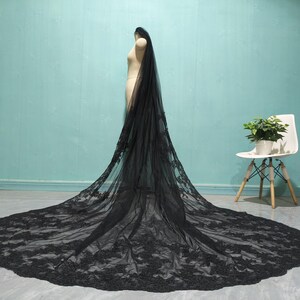 May include: A black lace wedding veil with a long train. The veil is made of soft tulle and features delicate floral lace.