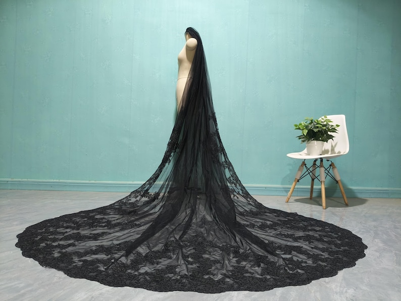 May include: A black lace wedding veil with a long train. The veil is made of soft tulle and features delicate floral lace.