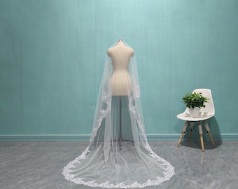May include: A white bridal veil with a delicate lace trim. The veil is long and flowing, and it is displayed on a mannequin.